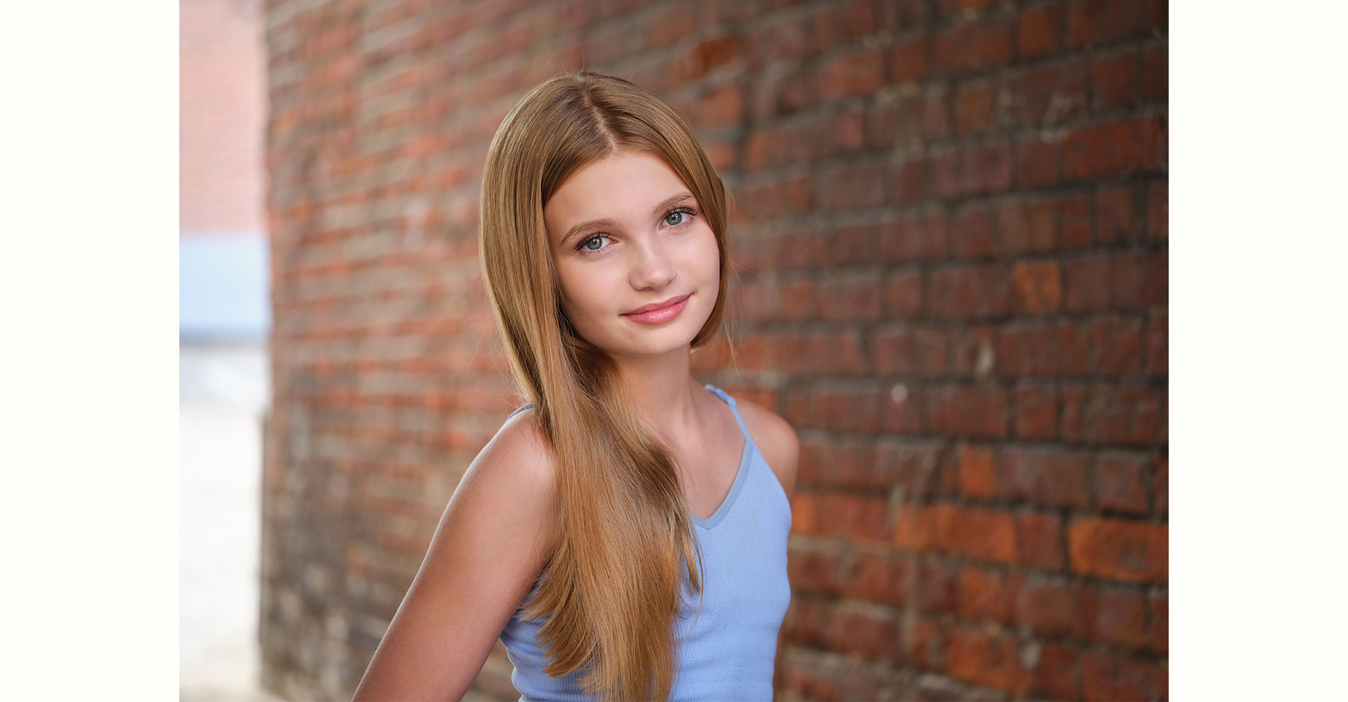 Teenage girl with long blonde hair headshot portrait front of brick wall